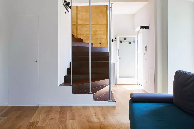 Interno di una casa unifamiliare moderna con scala in resina effetto ruggine e parquet in rovere chiaro, progettata da [Nome studio di architettura]. Il design è moderno e minimalista, con la scala che funge da elemento focale dell'ambiente.