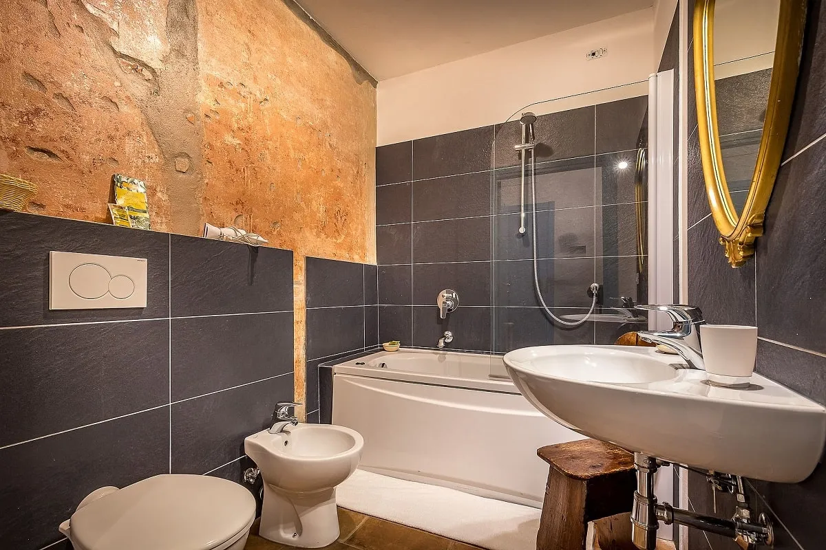 Bagno di una suite in un agriturismo con pareti in pietra originaria e rivestimenti contemporanei grigi, esempio di design tra antico e contemporaneo firmato Alitini Design