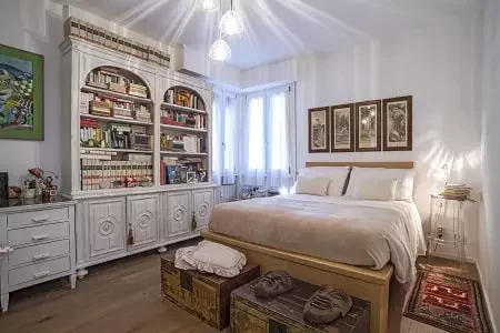 Questa camera da letto, parte di una casa ristrutturata con cura, unisce stile vintage e modernità. La libreria integrata offre un tocco classico, mentre le lampade a sospensione dal soffitto sostituiscono le tradizionali abat-jour creando un'atmosfera moderna e sofisticata. Il progetto di ristrutturazione ha sapientemente valorizzato gli spazi, creando un ambiente elegante e funzionale
